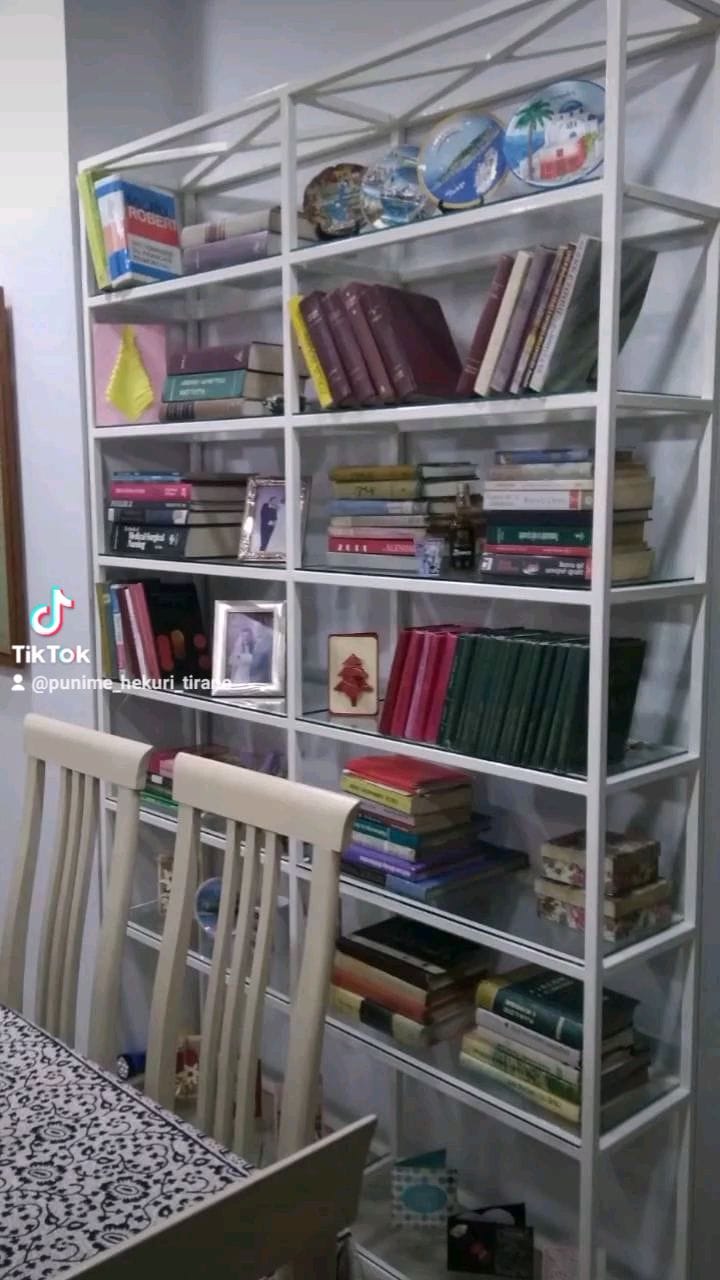 Bibliotekë metalike e bardhë me rafte xhami, e mbushur me libra